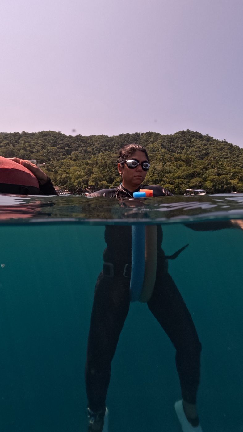 Apneísta con goggles en la superficie sujetando un tubo de foami, con un cerro de selva al fondo