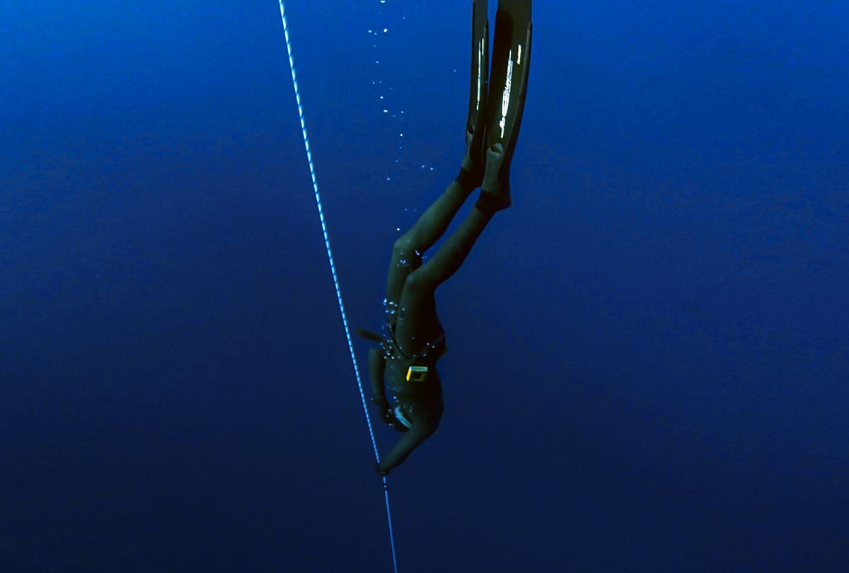Apneísta bajando de cabeza por un cabo en agua azul profunda