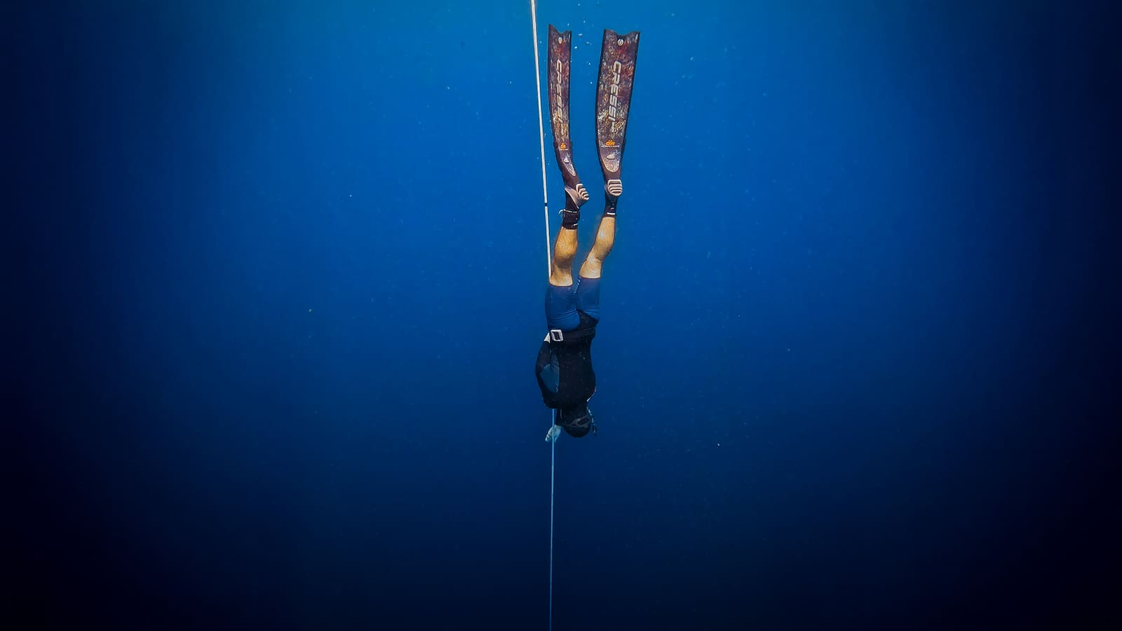Apneísta de cabeza en un cabo en agua azul profunda, con aletas de camuflaje arriba