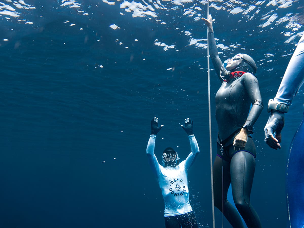 Freediver surfacing with arms raised beside the line as a second diver holds it