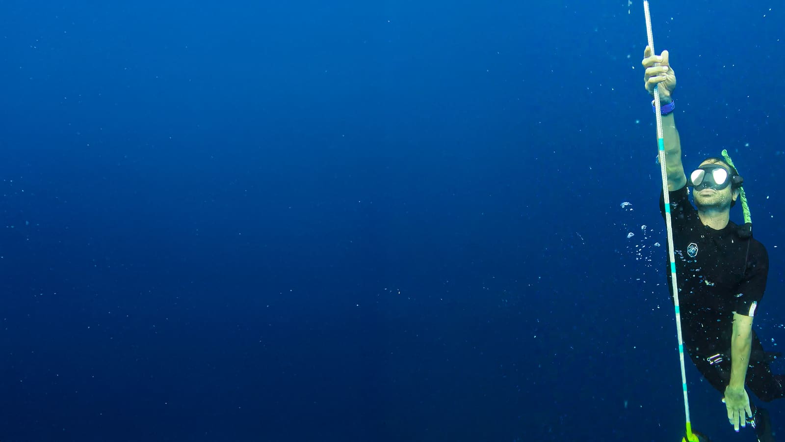 Freediver in a mask and nose clip pulling up a line in open blue water