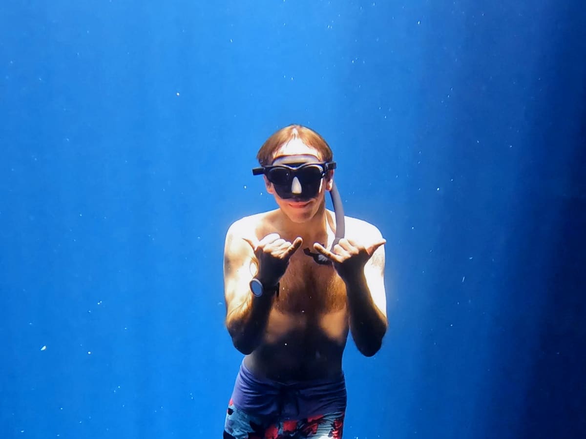 Snorkeler underwater in a mask making shaka signs with both hands